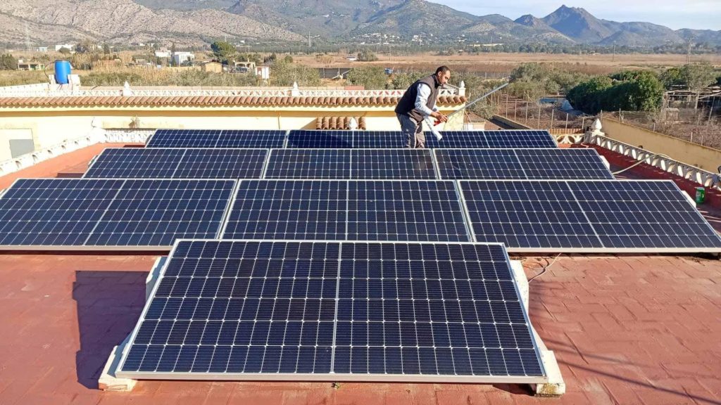 Hombre instalando paneles solares en un tejado de tejas rojas con vistas a la montaña de fondo Castellón y Valencia